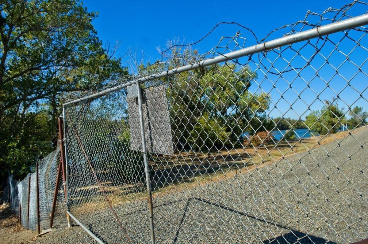 A cross-levee fence blocks access along the Sacramento River in the Pocket neighborhood of Sacramento in 2019. Similar fences have become a point of contention as Sacramento pursues plans for a Sacramento River Parkway trail.